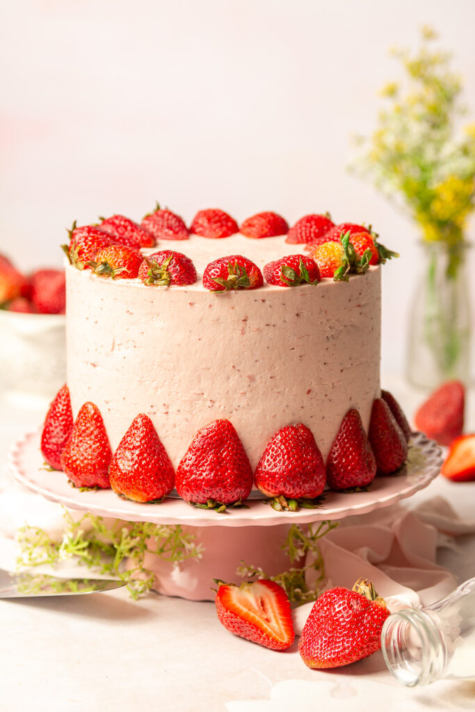 triple strawberry layer cake decorated with fresh halved strawberries on a cake stand