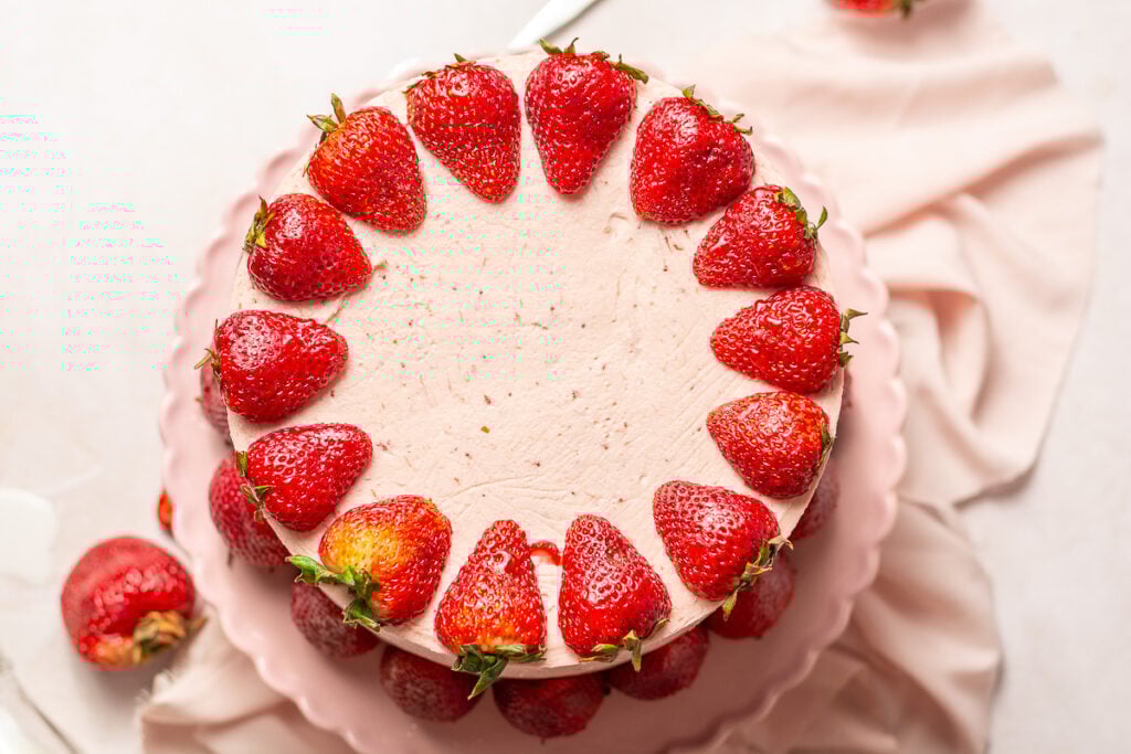 triple strawberry layer cake decorated with fresh halved strawberries on a cake stand