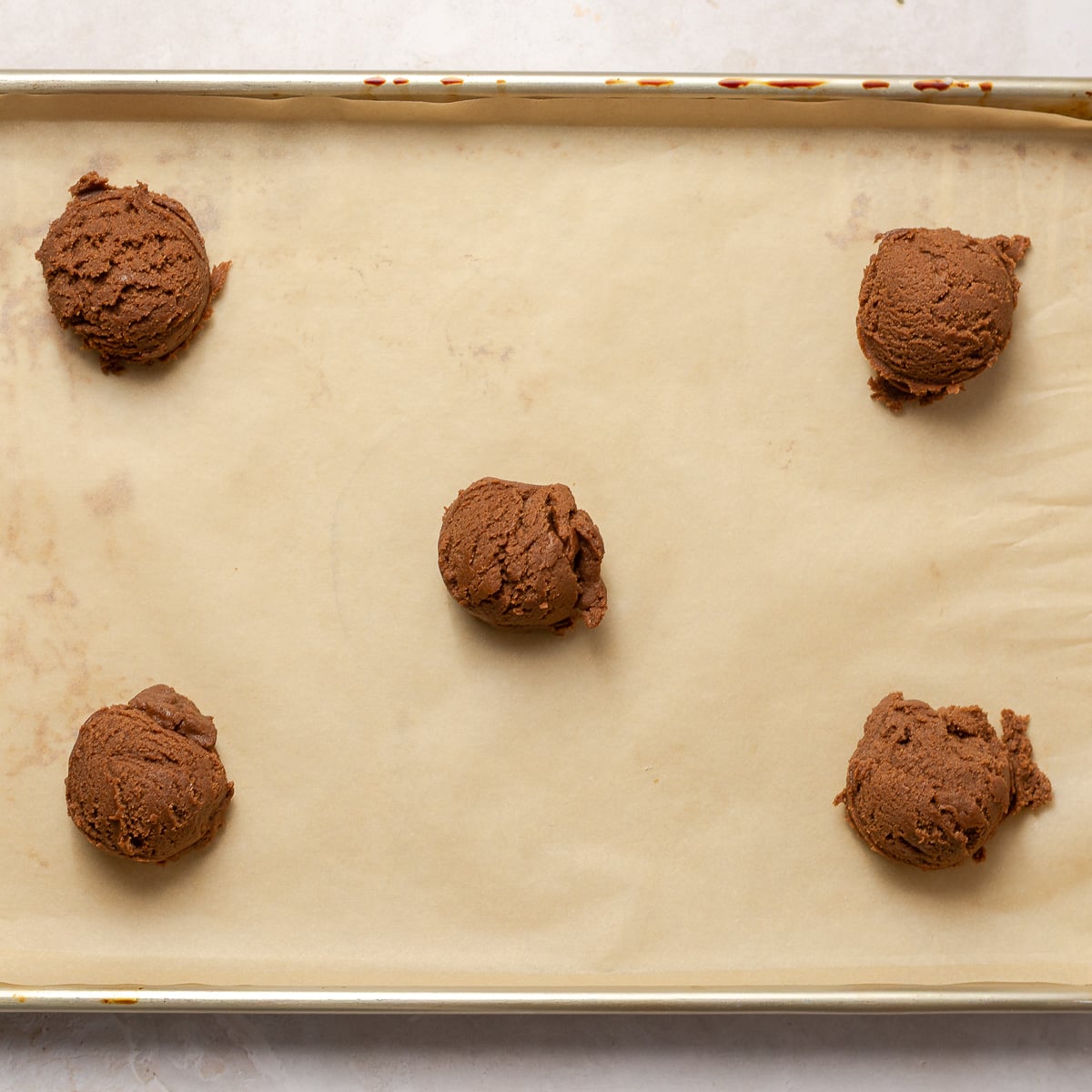 5 scoops of chocolate cookie dough arranged on a parchment lined baking sheet.