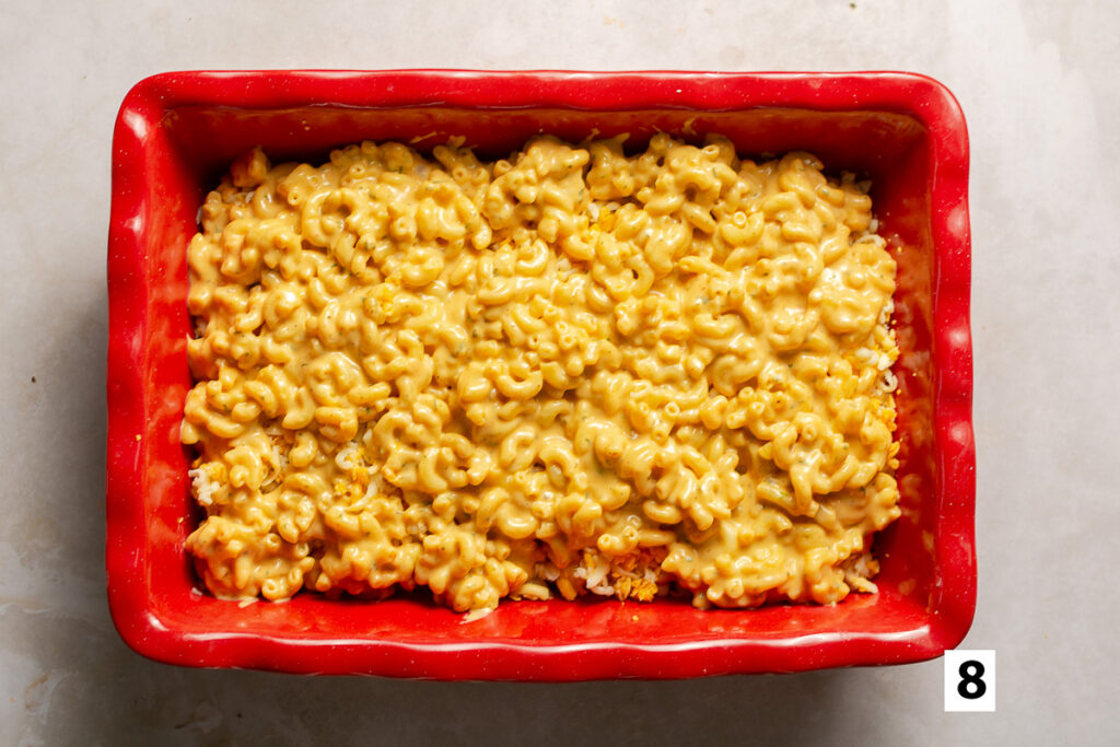 layering shredded cheese in a casserole dish with cheesy elbow macaroni for a baked mac & cheese
