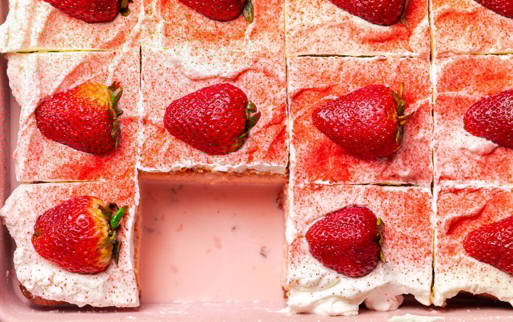 strawberry tres leches cake in a pink pan garnished with a dusting of freeze-dried strawberries and halved fresh strawberries