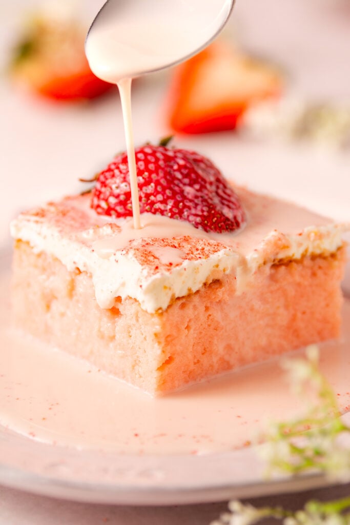 slice of strawberry tres leches cake on a plate with tres leches milk mixture