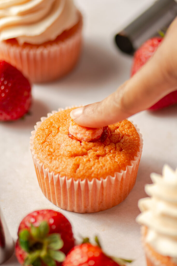covering the filling of a strawberry cupcake with a piece of cake
