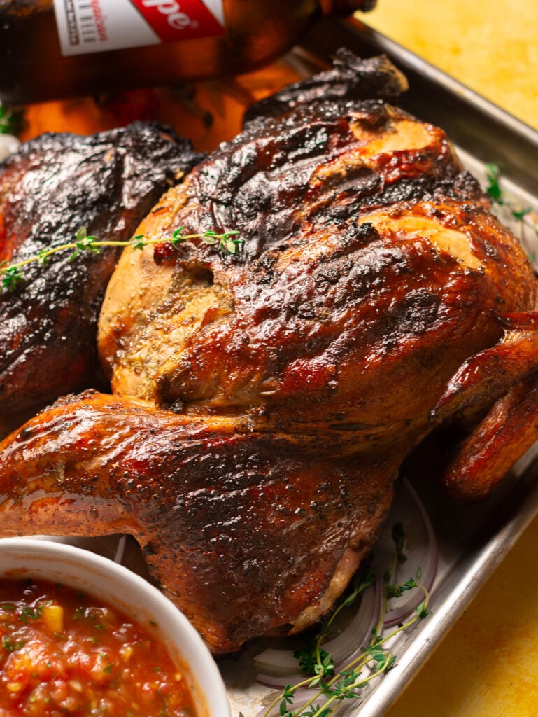 whole jerk chicken on a metal baking tray with a bottle of Red Stripe beer