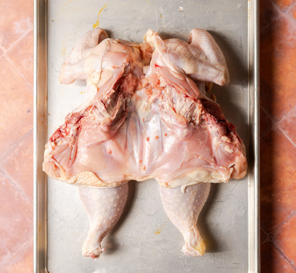 spatchcocked chicken breast-side down on a metal baking tray