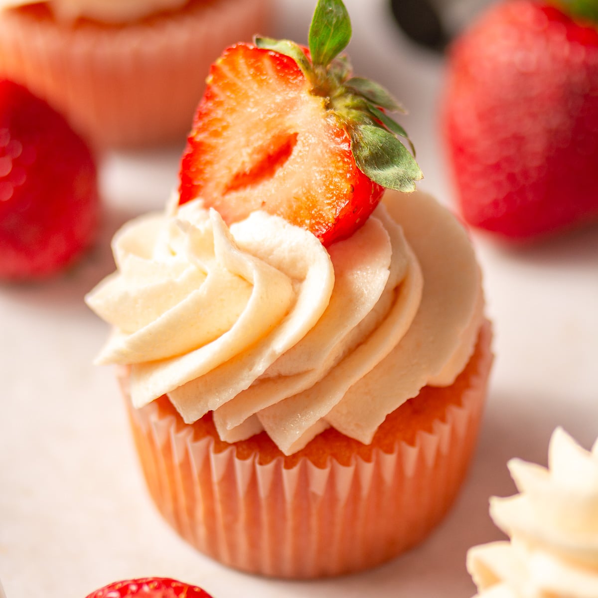 strawberry cupcake with strawberry frosting garnished with half of a strawberry.