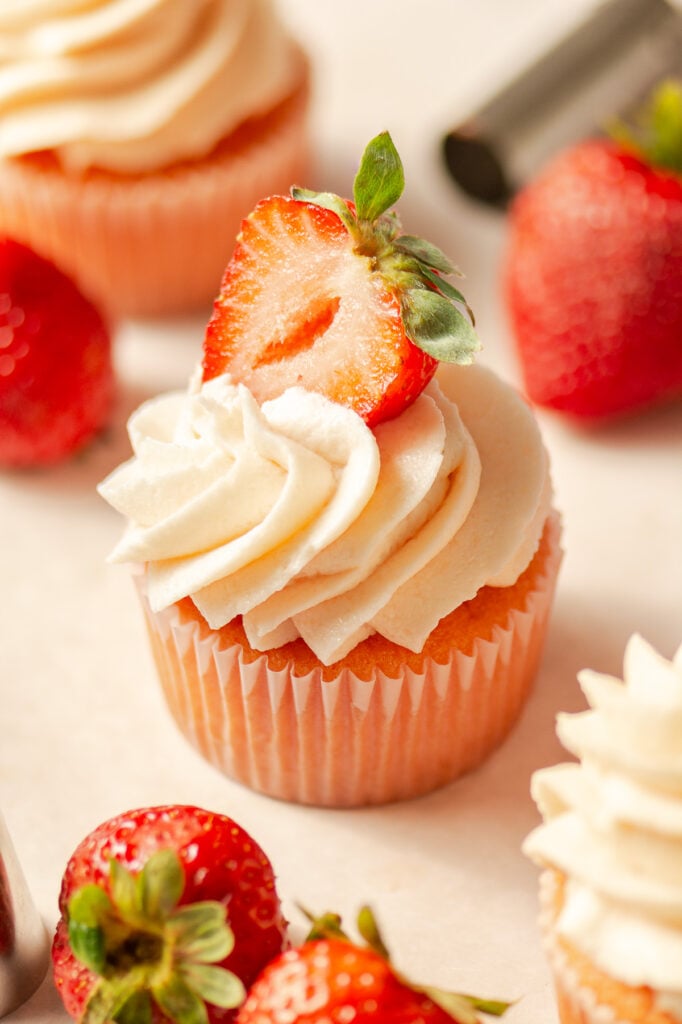 strawberry cupcakes topped with strawberry buttercream and half of a fresh strawberry