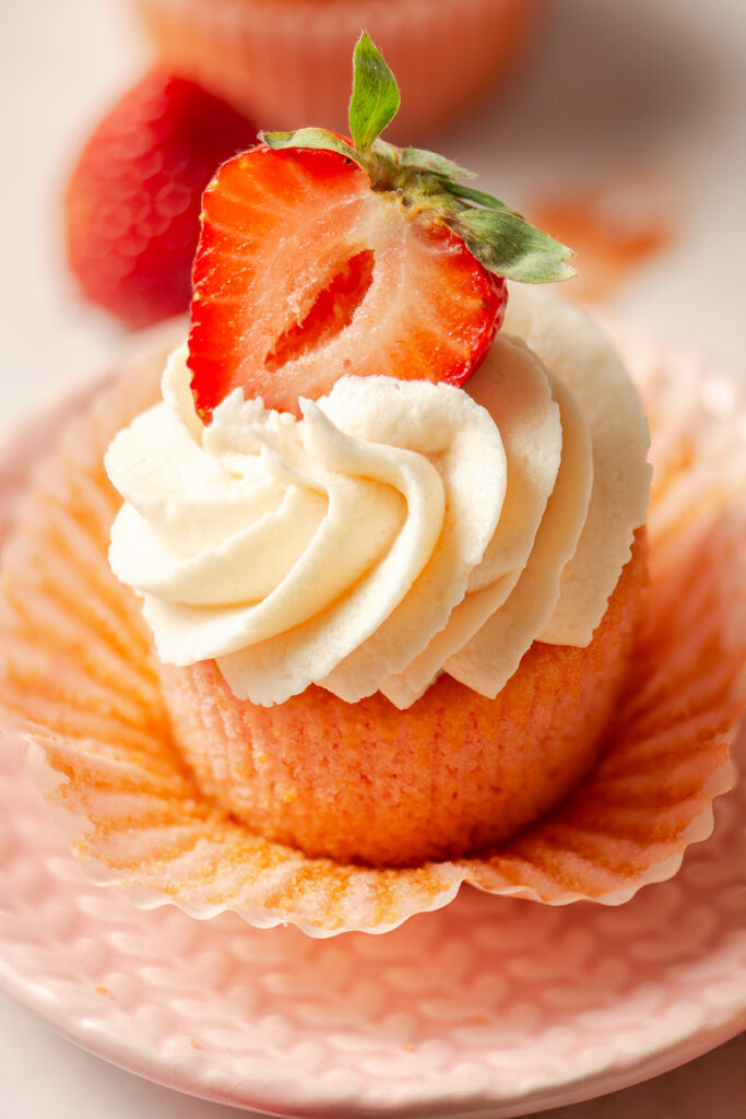 strawberry cupcakes topped with strawberry buttercream and half of a fresh strawberry