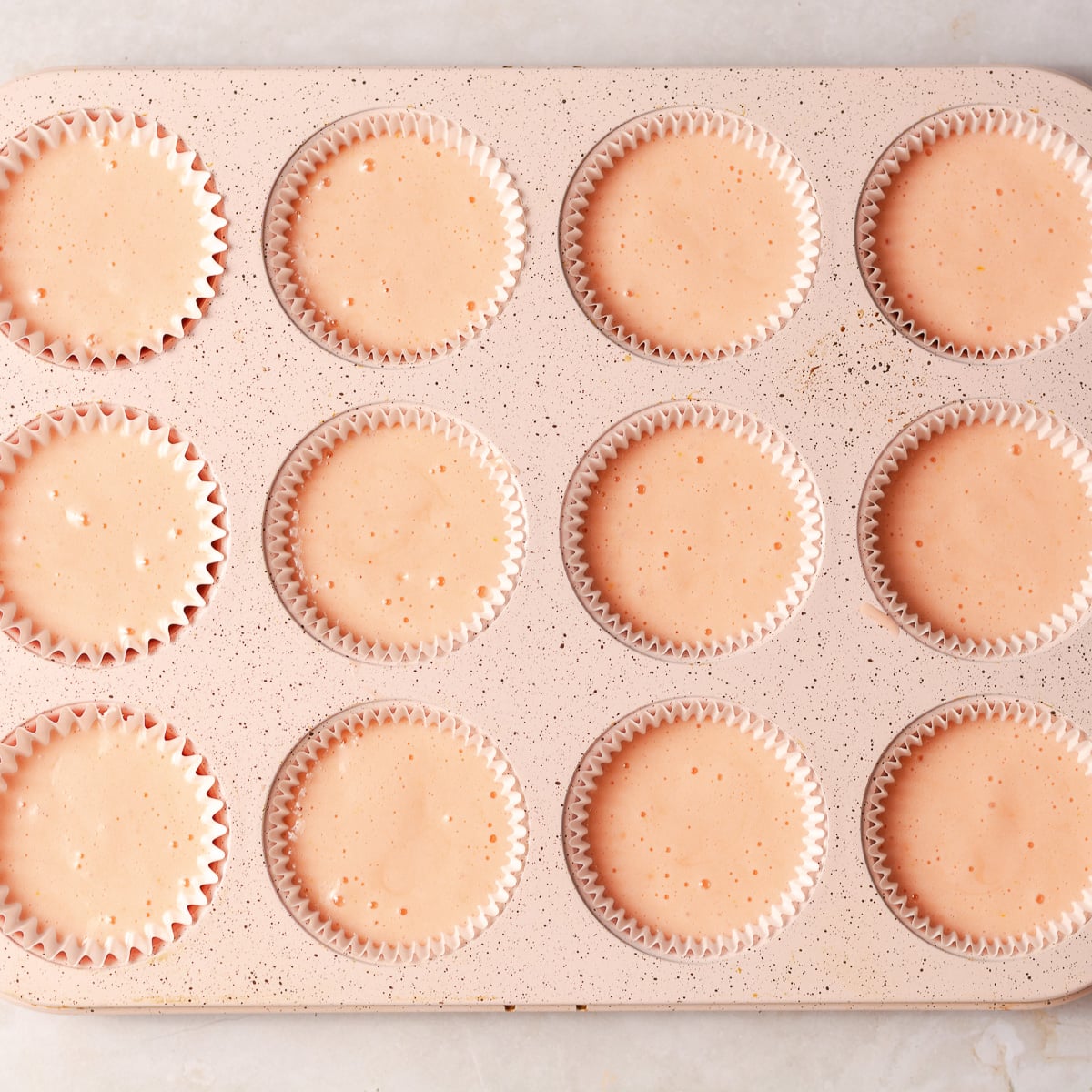cupcake liners in a cupcake baking pan filled with strawberry cupcake batter.