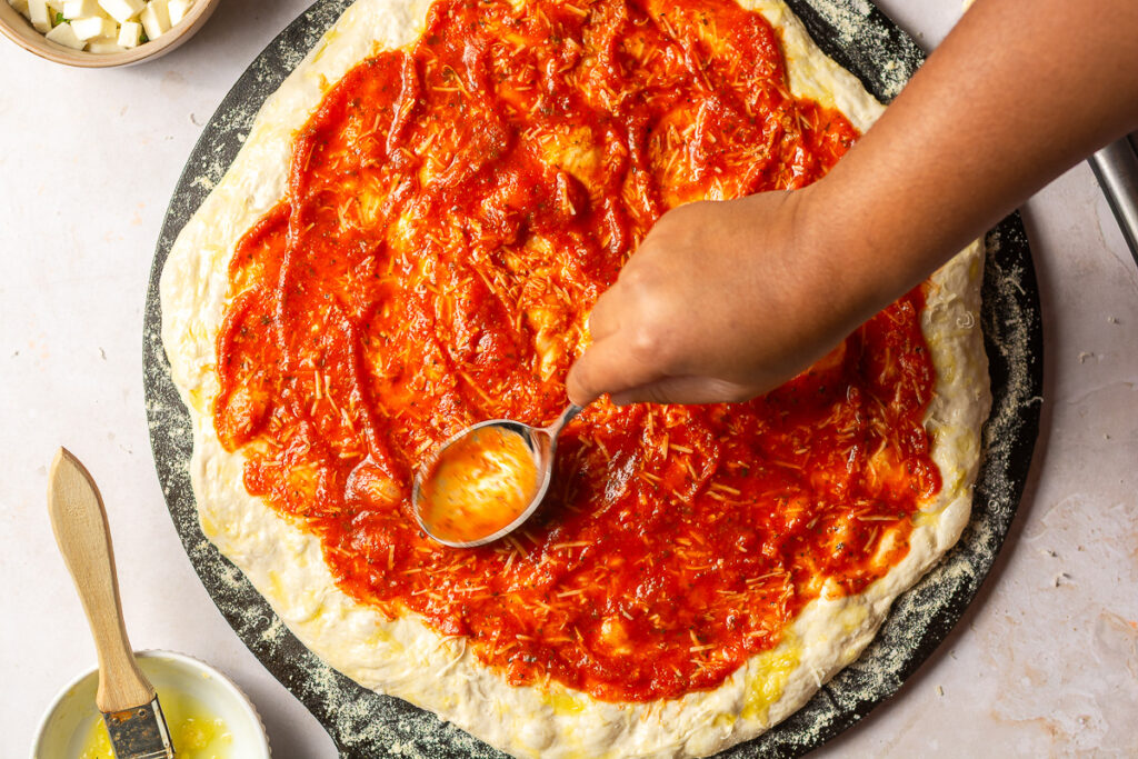 spreading marinara sauce on homemade pizza dough