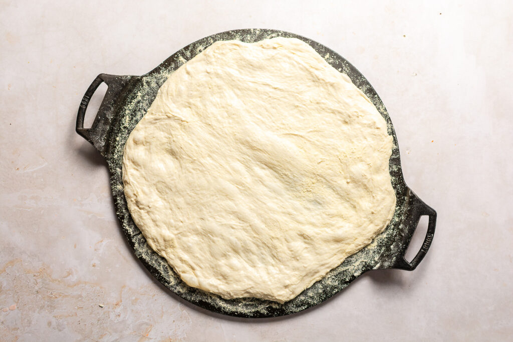 homemade pizza dough stretched into a circle on cast iron griddle