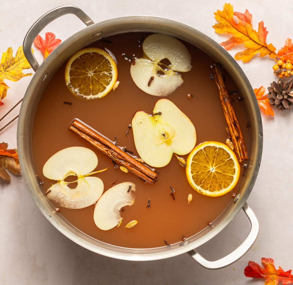 stockpot filled with mulled apple cider and garnished with apple and orange slices, cinnamon sticks & whole cloves