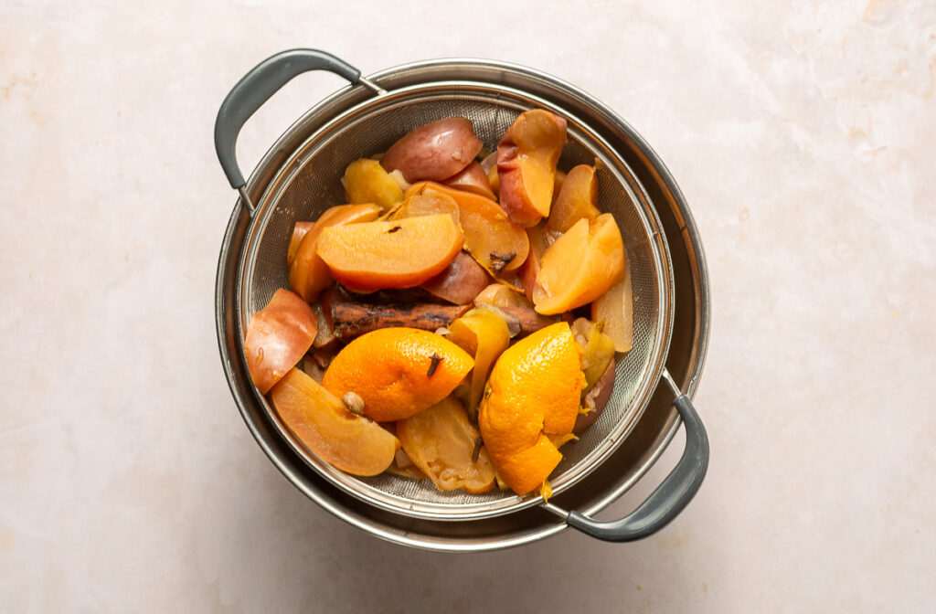 mulled cider strained into a bowl to separate the apples, oranges, cinnamon sticks, cloves and cardamom pods