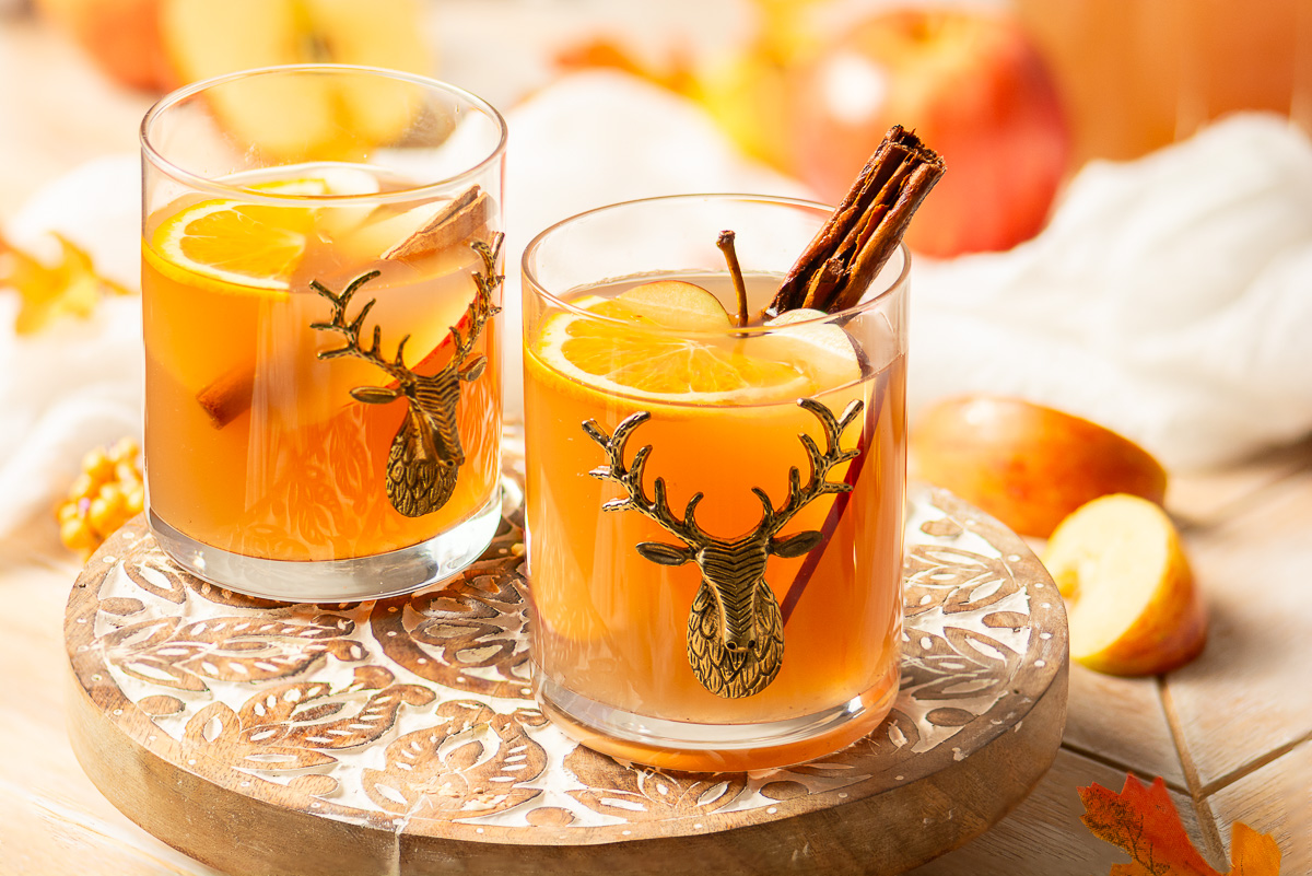 two glasses of mulled apple cider on a wooden serving tray
