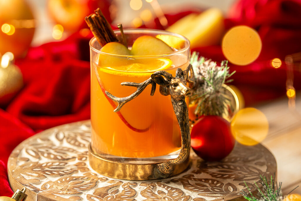 glass of mulled apple cider with a slice of orange and apple and a cinnamon stick as garnish