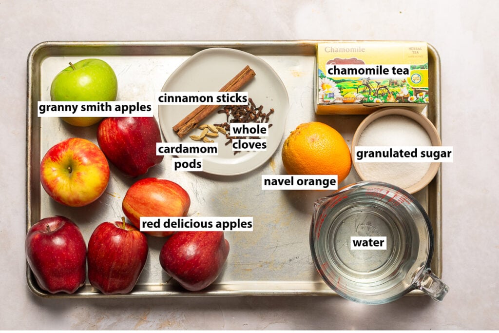 ingredients for mulled apple cider - granny smith apples, red delicious apple, cinnamon sticks, whole cloves, cardamom pods, navel orange, chamomile tea, granulated sugar & water