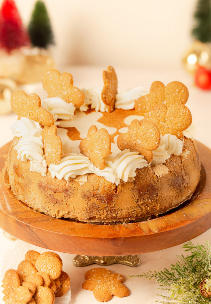 ginger bread cheesecake with brown sugar whipped cream and gingerbread men decorations on a wooden cake stand