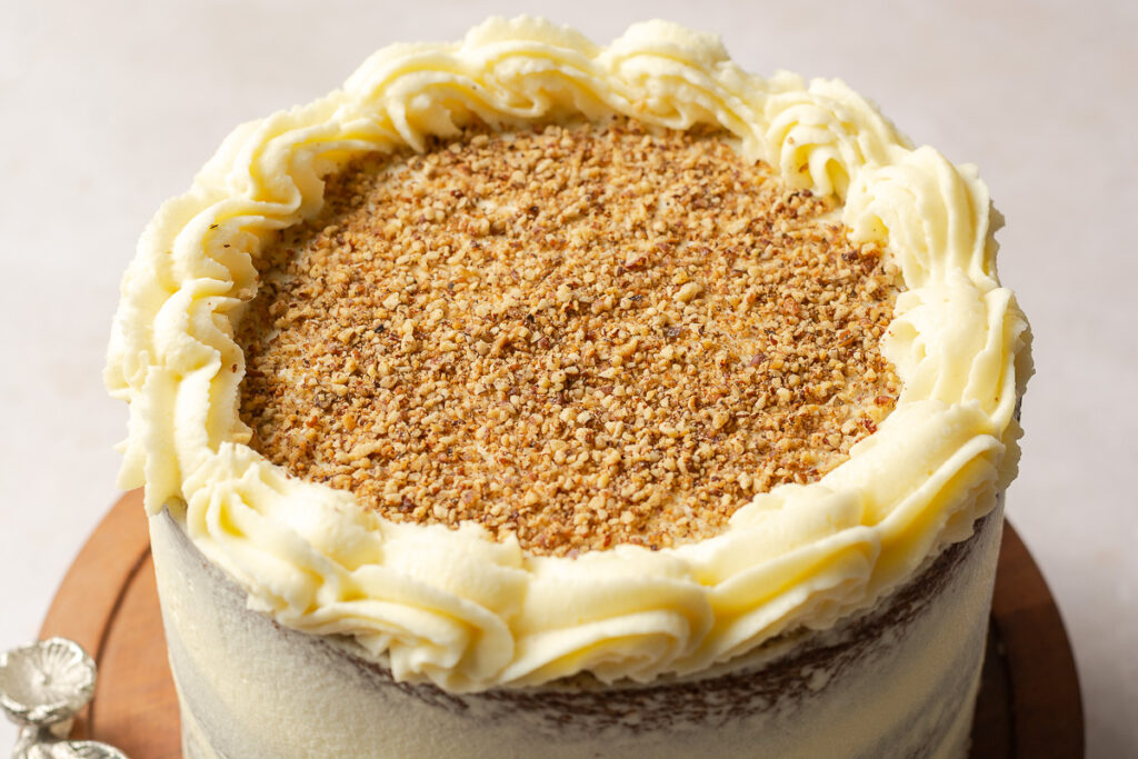 cream cheese border with crushed toasted pecans on top of a hummingbird layer cake