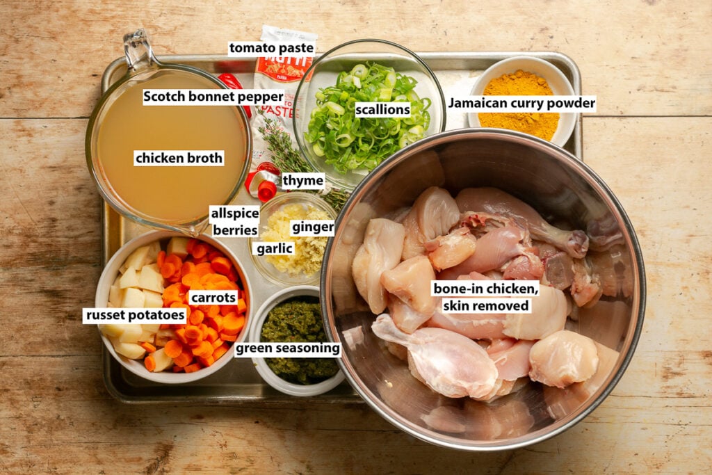 ingredients for Jamaican curry chicken - Jamaican curry powder, bone-in & skinless chicken, green seasoning, potatoes, carrots, thyme, garlic, ginger, allspice berries, Scotch bonnet pepper, scallions, tomato paste & chicken broth