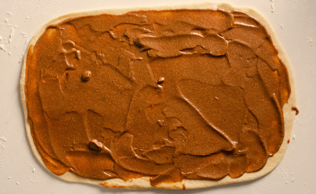 cinnamon roll dough rolled out in counter and spread with banana-cinnamon filling