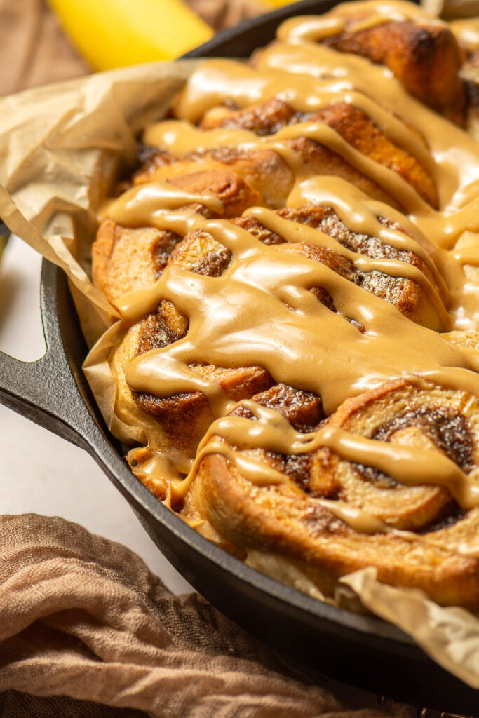 banana cinnamon rolls with brown sugar cream cheese frosting in a cast iron pan