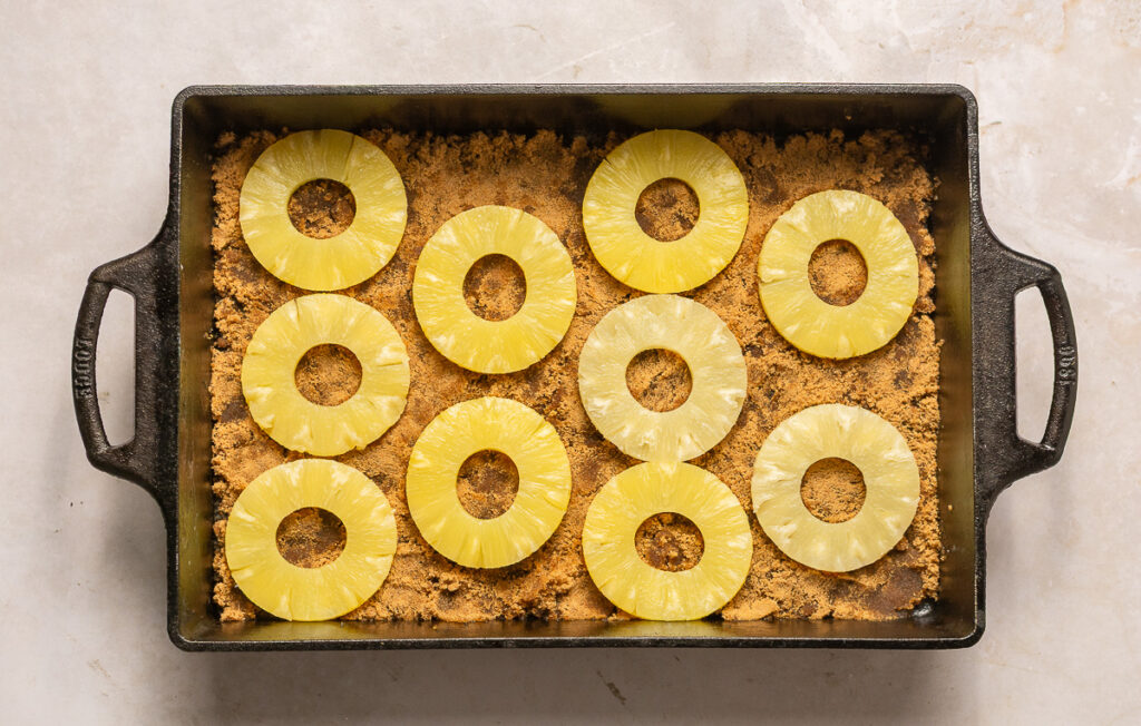 pineapple slices in a cast iron baking dish packed with brown sugar