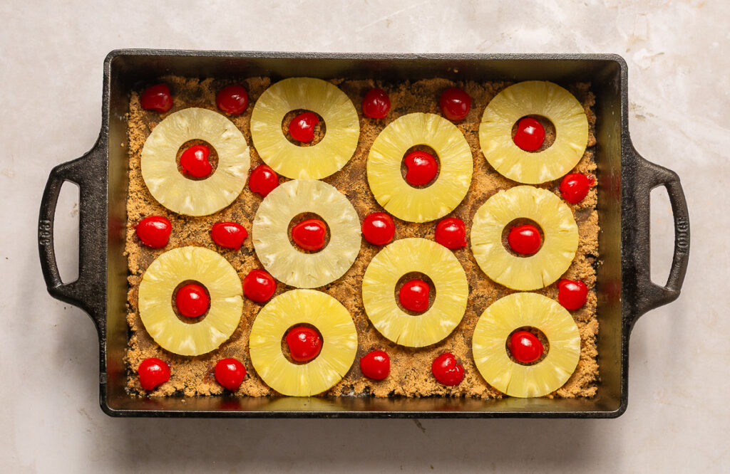 pineapple slices and maraschino cherries arranged in a cast iron pan for a pineapple upside-down cake