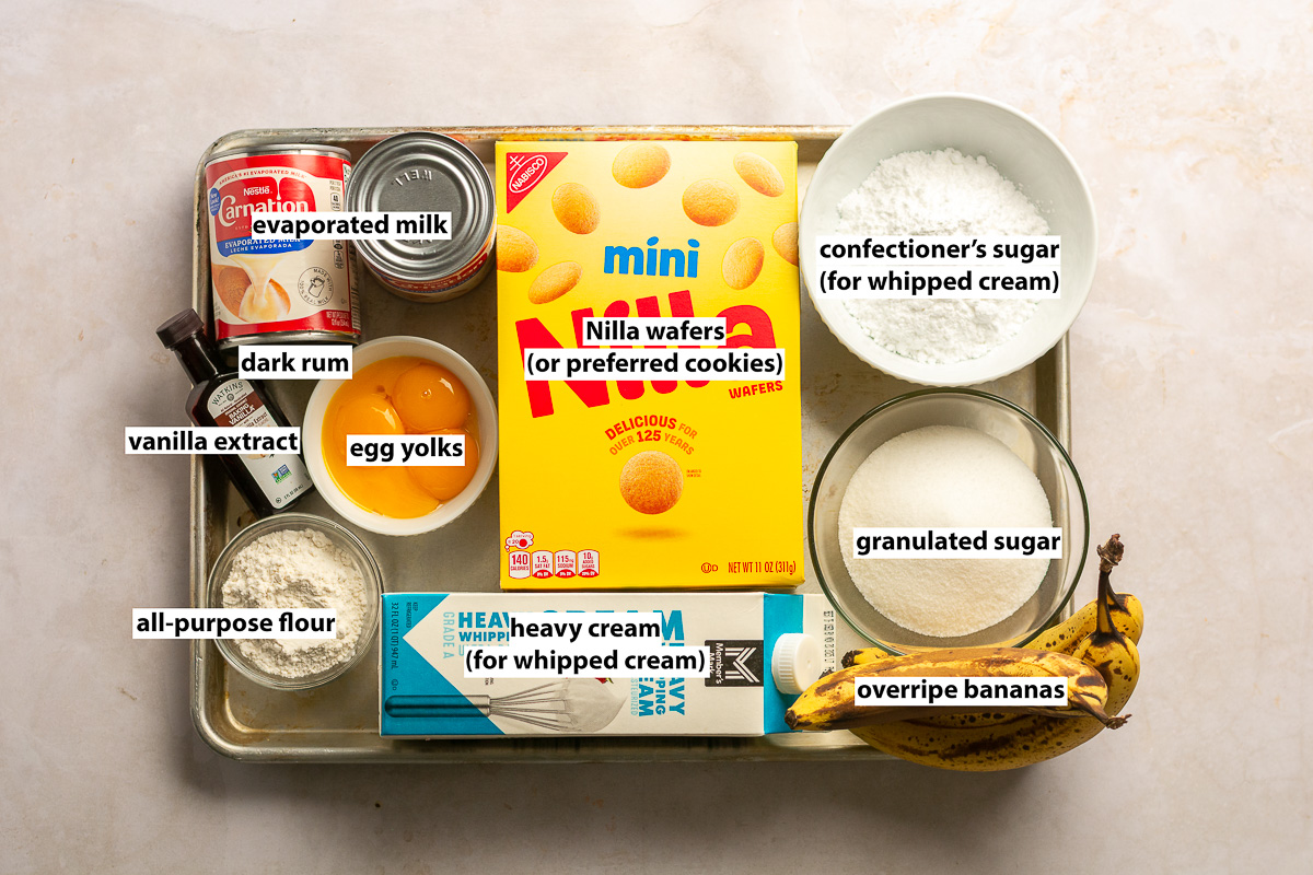 ingredients to make banana pudding from scratch - overripe bananas, egg yolks, evaporated milk, all-purpose flour, granulated sugar, Nilla wafers, vanilla extract, dark rum, heavy cream, and confectioner's sugar.