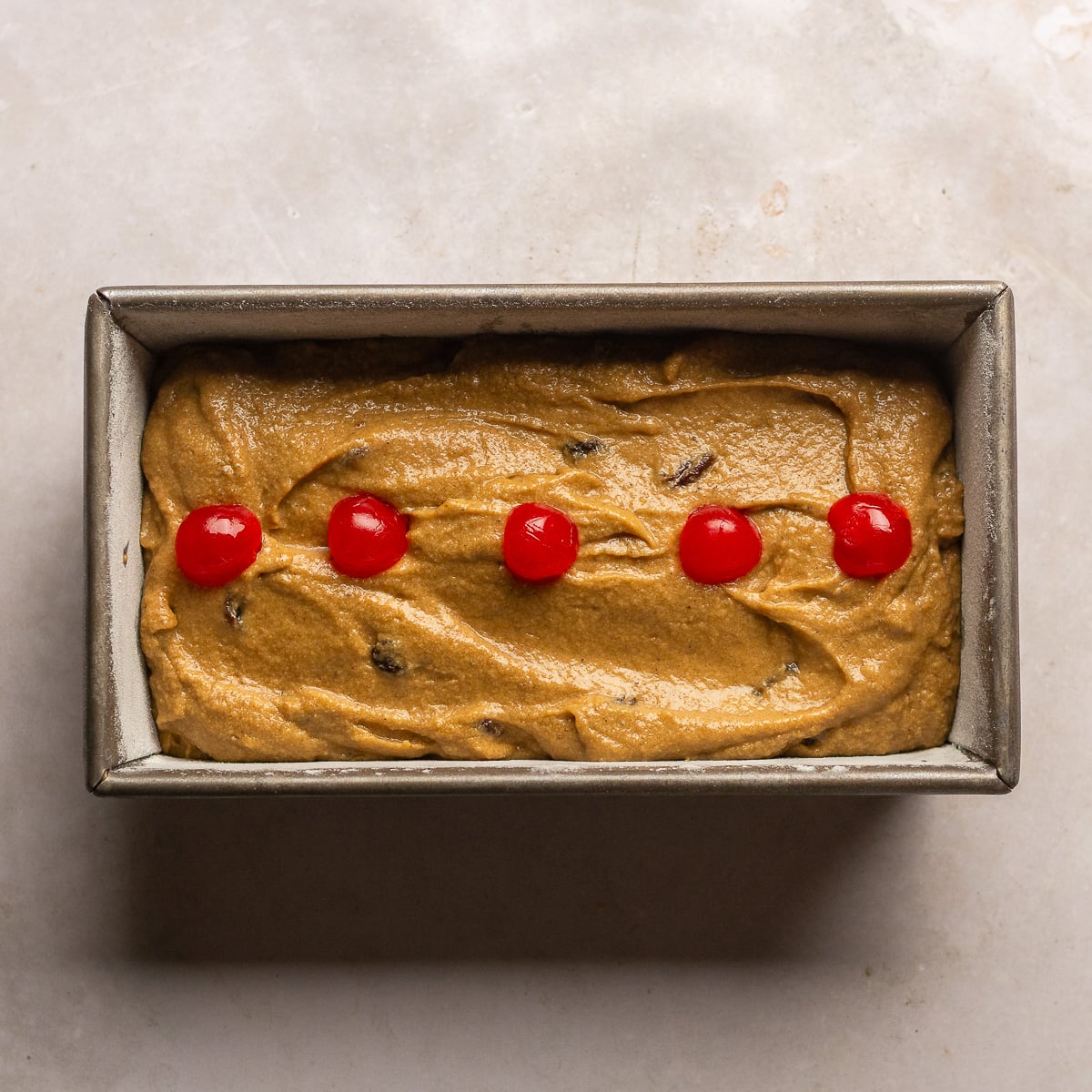 Jamaican Easter bun batter topped with halved Maraschino cherries in a loaf pan.