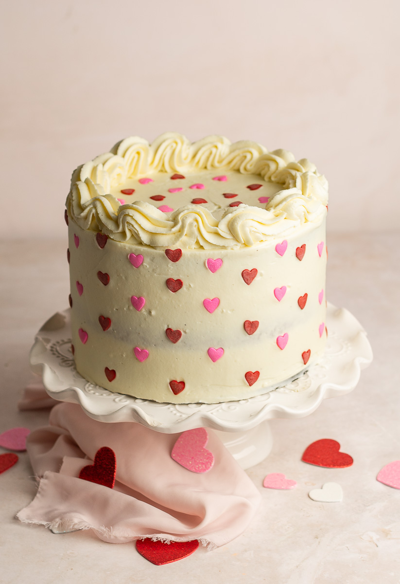 red velvet layer cake decorated with cream cheese frosting and heart shaped sprinkles.
