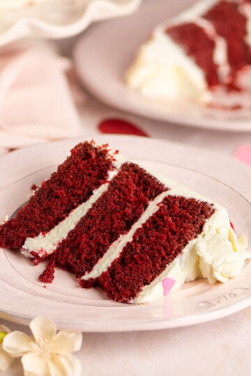 slice of red velvet layer cake with cream cheese frosting on a plate.