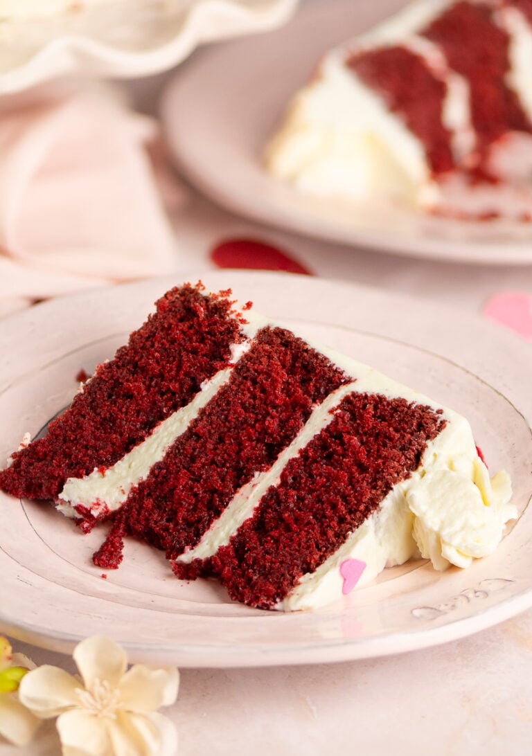 slice of red velvet layer cake with cream cheese frosting on a plate.