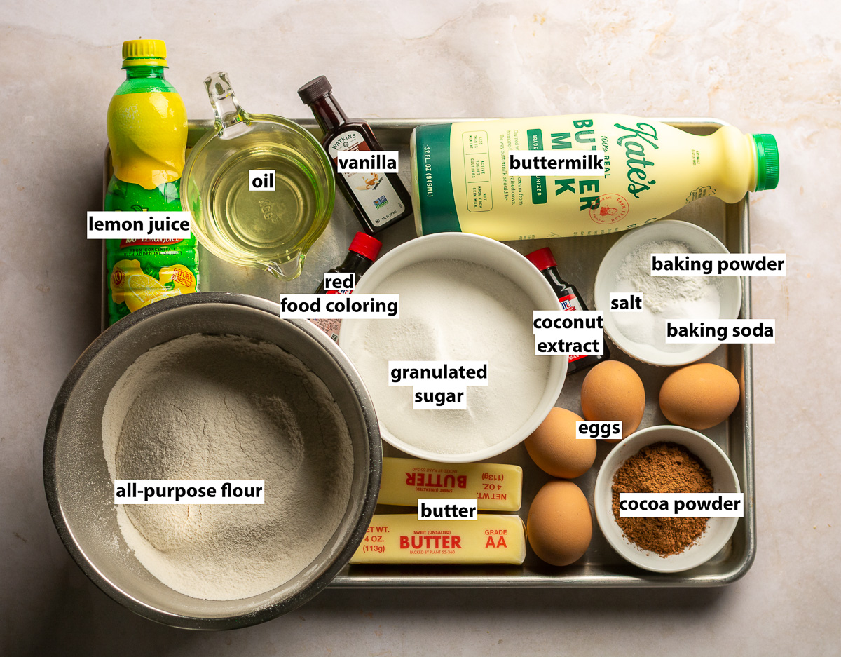 ingredients for red velvet layer cake - all-purpose flour, granulated sugar, buttermilk, lemon juice, butter, oil, eggs, vanilla, coconut extract, red food coloring, baking powder, salt and baking soda.