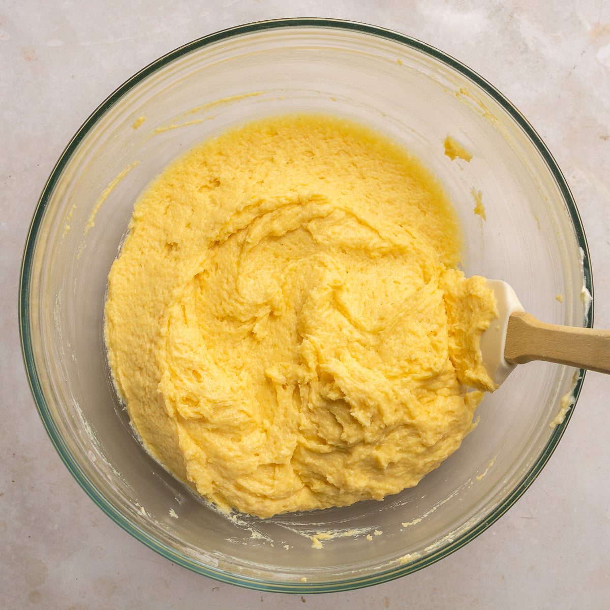 cornbread batter in a glass mixing bowl with a spatula.