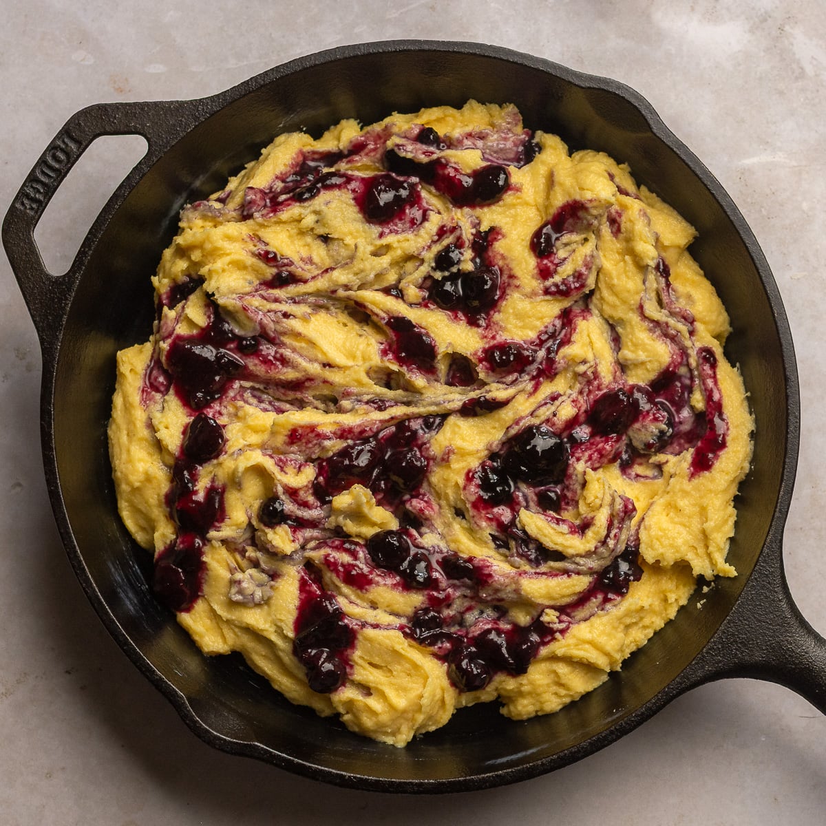 cornbread batter swirled with blueberry compote in a cast iron skillet.