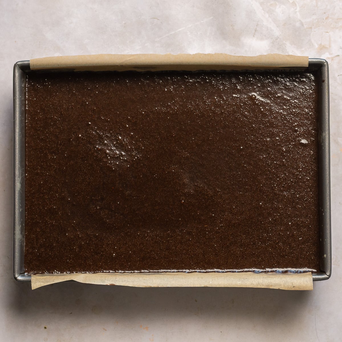 double chocolate cake batter in a 9x13 inch pan with a parchment paper sling.