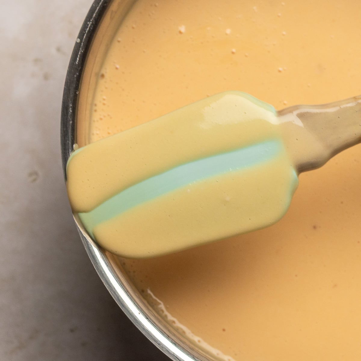 Spatula showing nappe consistency of thickened custard for strawberry cheesecake ice cream.