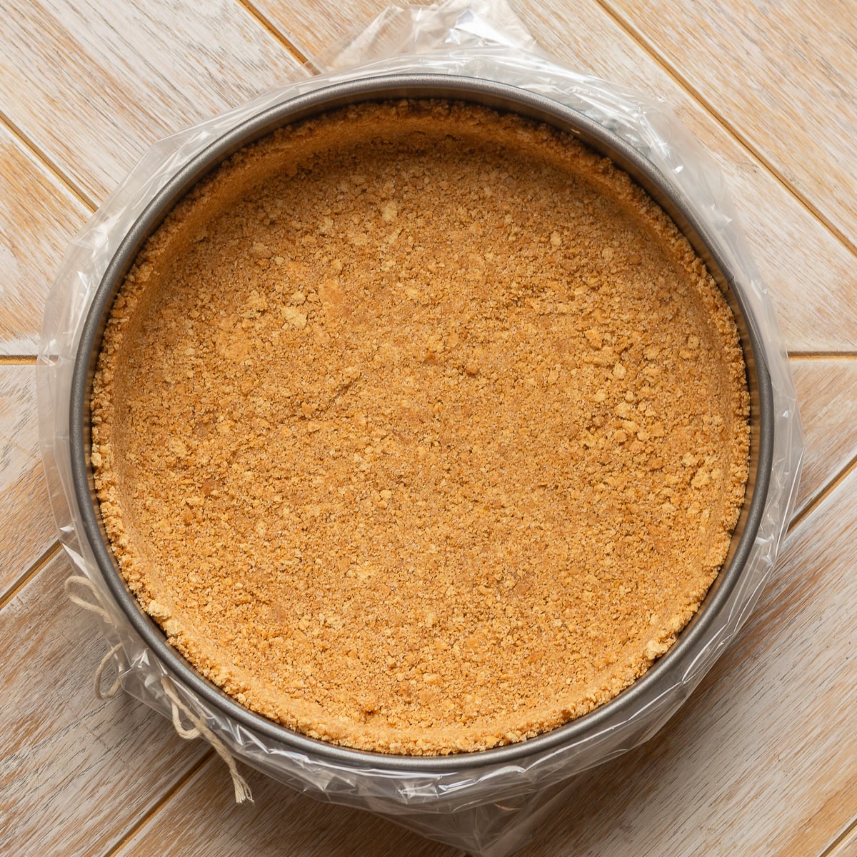 Springform pan with graham cracker crust prepared for water bath with oven bag.