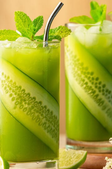 2 glasses of cucumber limeade garnished with a slice of cucumber and mint.