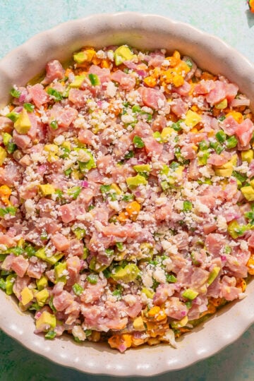 Layered fresh tuna dip with elote and guac in a pie dish.