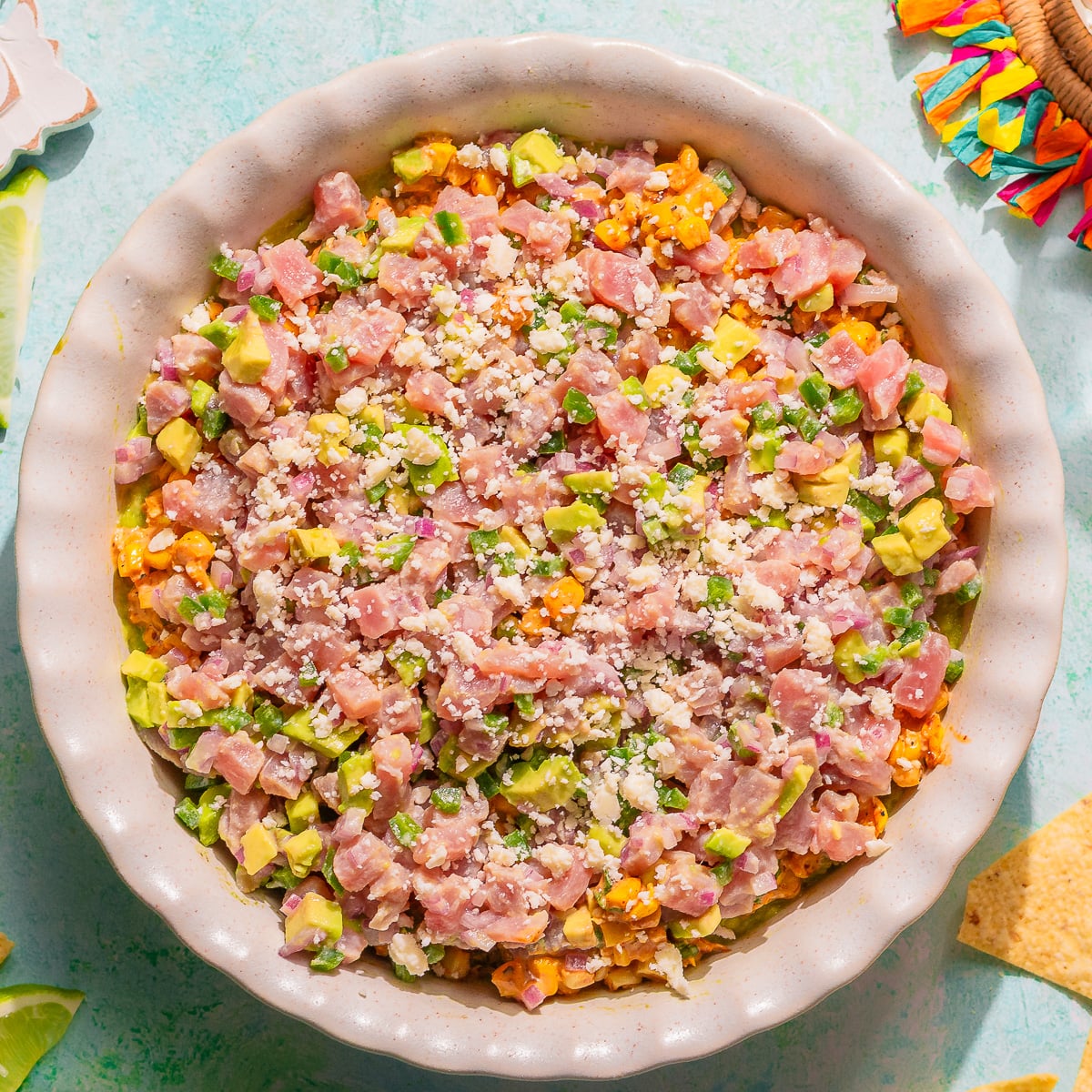 Layered fresh tuna dip with elote and guac in a pie dish.