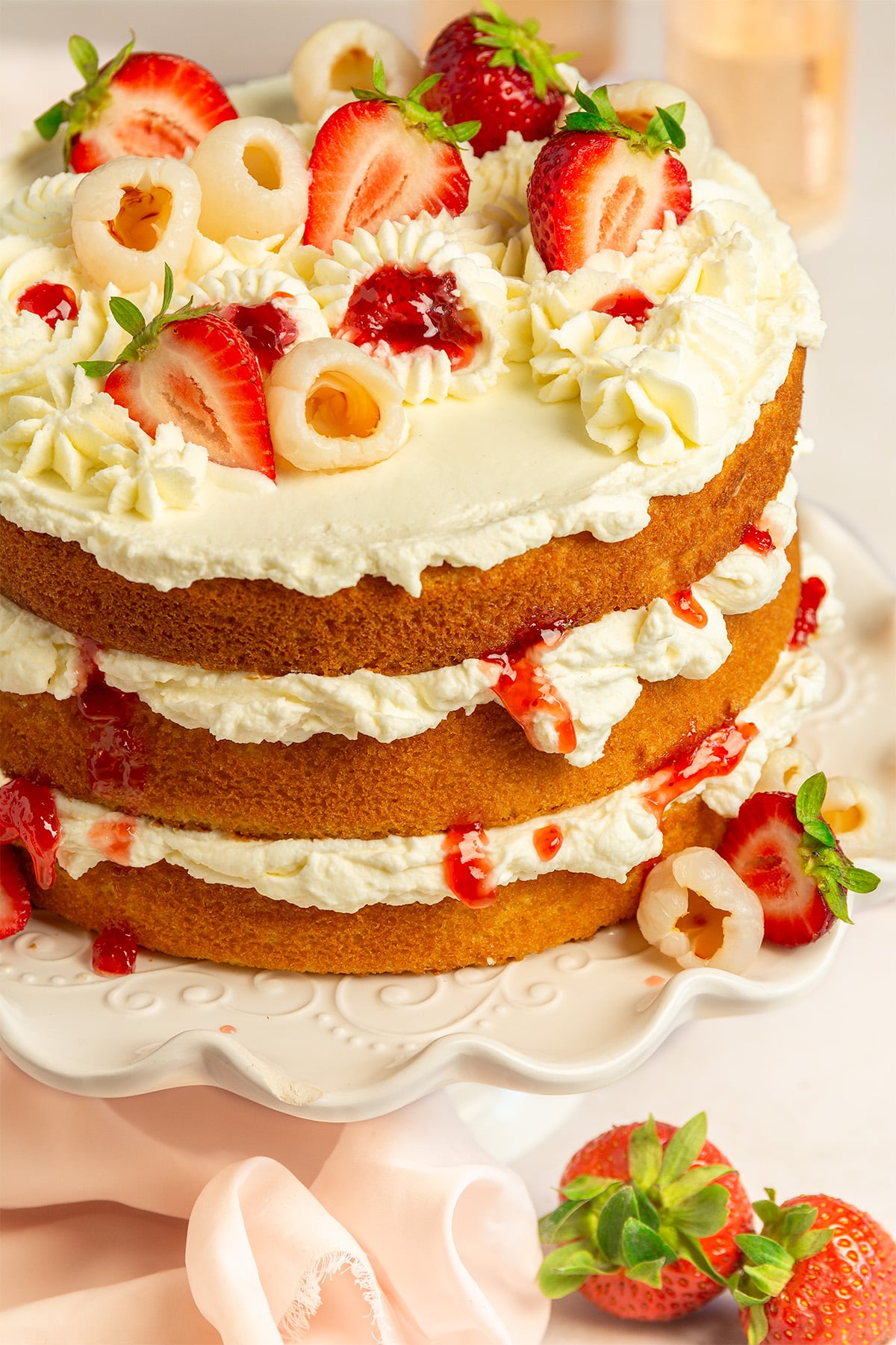 lychee cake layered with strawberry and lychee filling and Chantilly frosting on a cake stand.