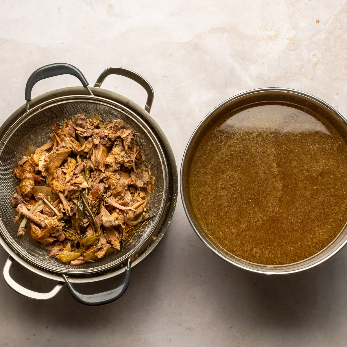 strained chicken stock in a bowl and leftover chicken carcass and vegetables in a strainer.