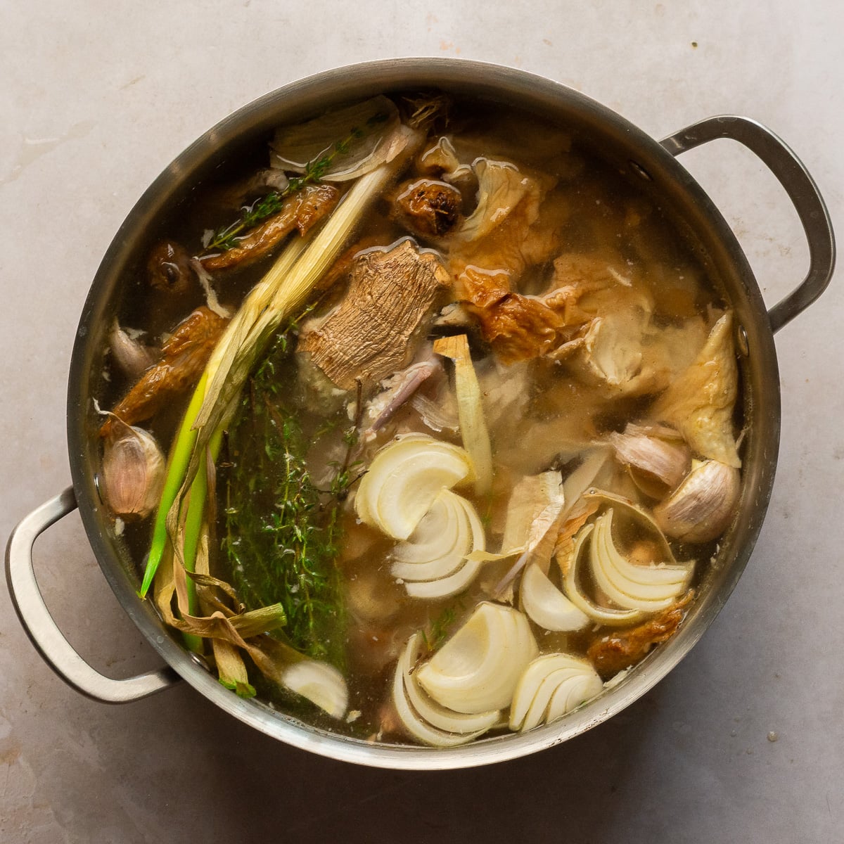 rotisserie chicken carcass with herbs, vegetables and water in a stockpot.